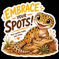 A die-cut sticker featuring a cartoon leopard gecko sitting on rocks with the text 'EMBRACE YOUR SPOTS!' and 'Your quirks make you shine.' on a black background.